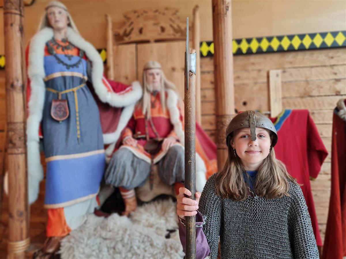 Jente med rustning og hjelm utkledd som viking med utstillingsdukker av Harald Hårfagre og Gyda - Klikk for stort bilde