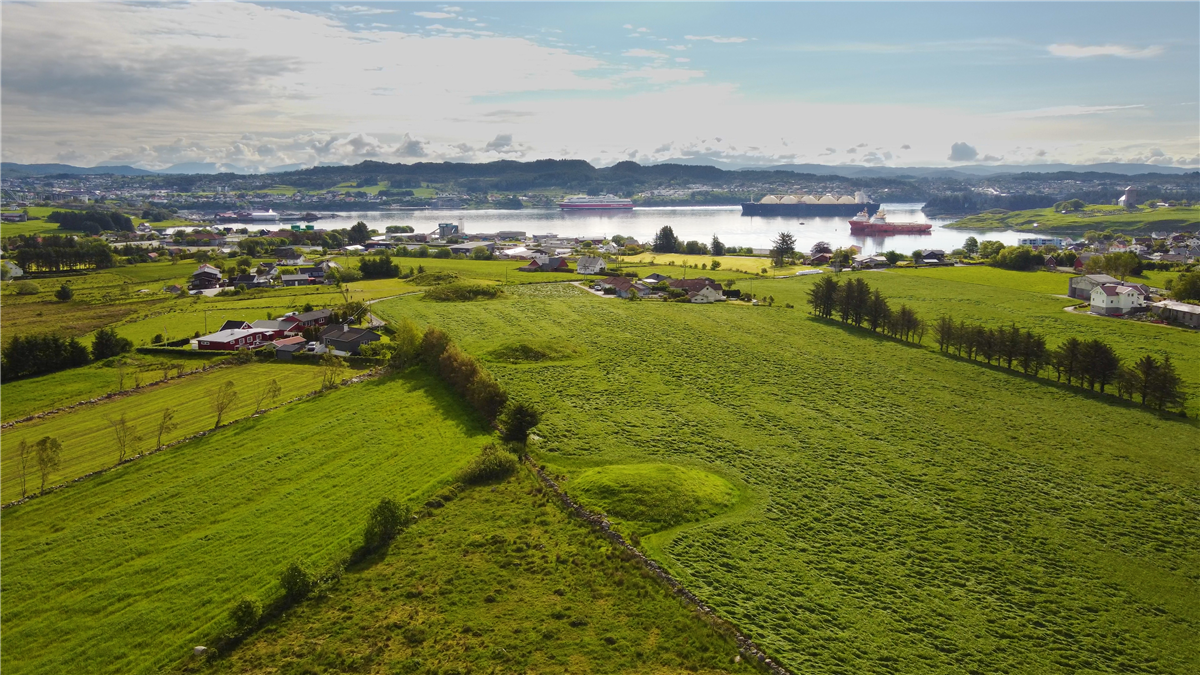 Dronefoto ovre Rehaugane på Torvastad der en ser omriss av gravhauger og Karmsundet - Klikk for stort bilde