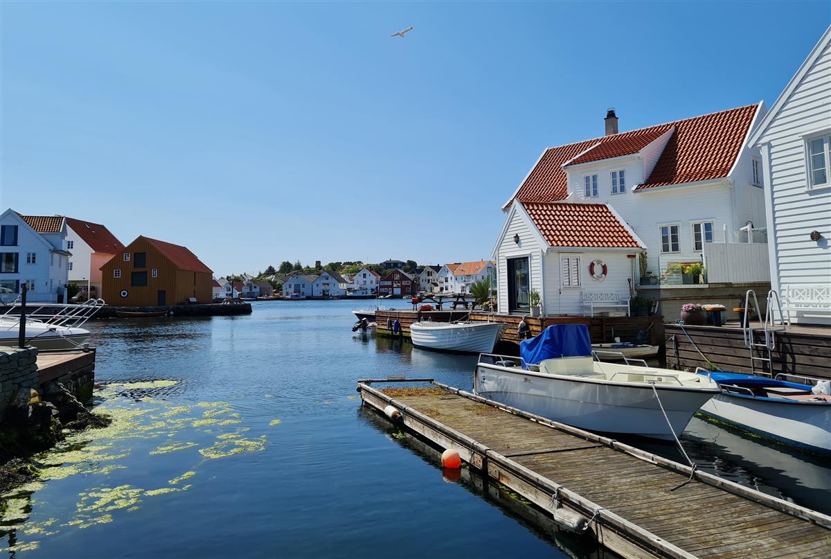 Havnebassenget med sjø, brygge, båt, trehvite hus i Skudeneshavn - Klikk for stort bilde
